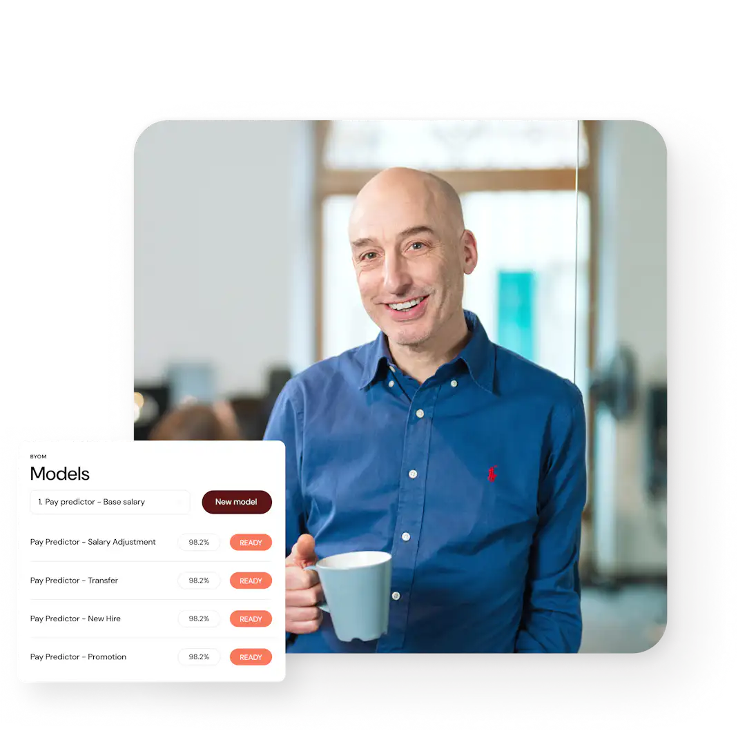 Homme souriant portant une chemise bleue, tenant une tasse, avec un fond flou montrant un espace de travail.