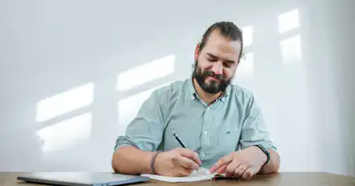 Homme assis à un bureau en train d'écrire dans un cahier.