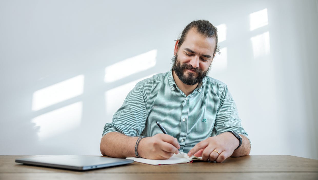 Homme assis à un bureau en train d'écrire dans un cahier.