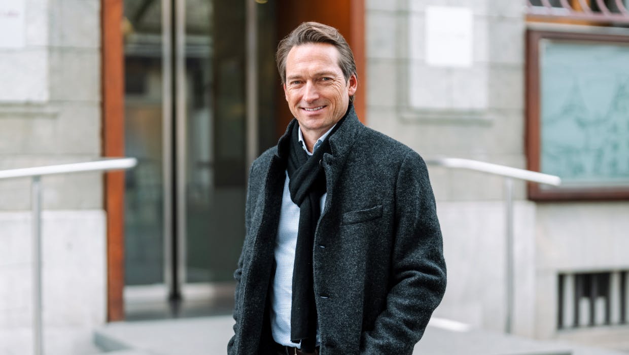 Homme en veste debout devant un bureau.