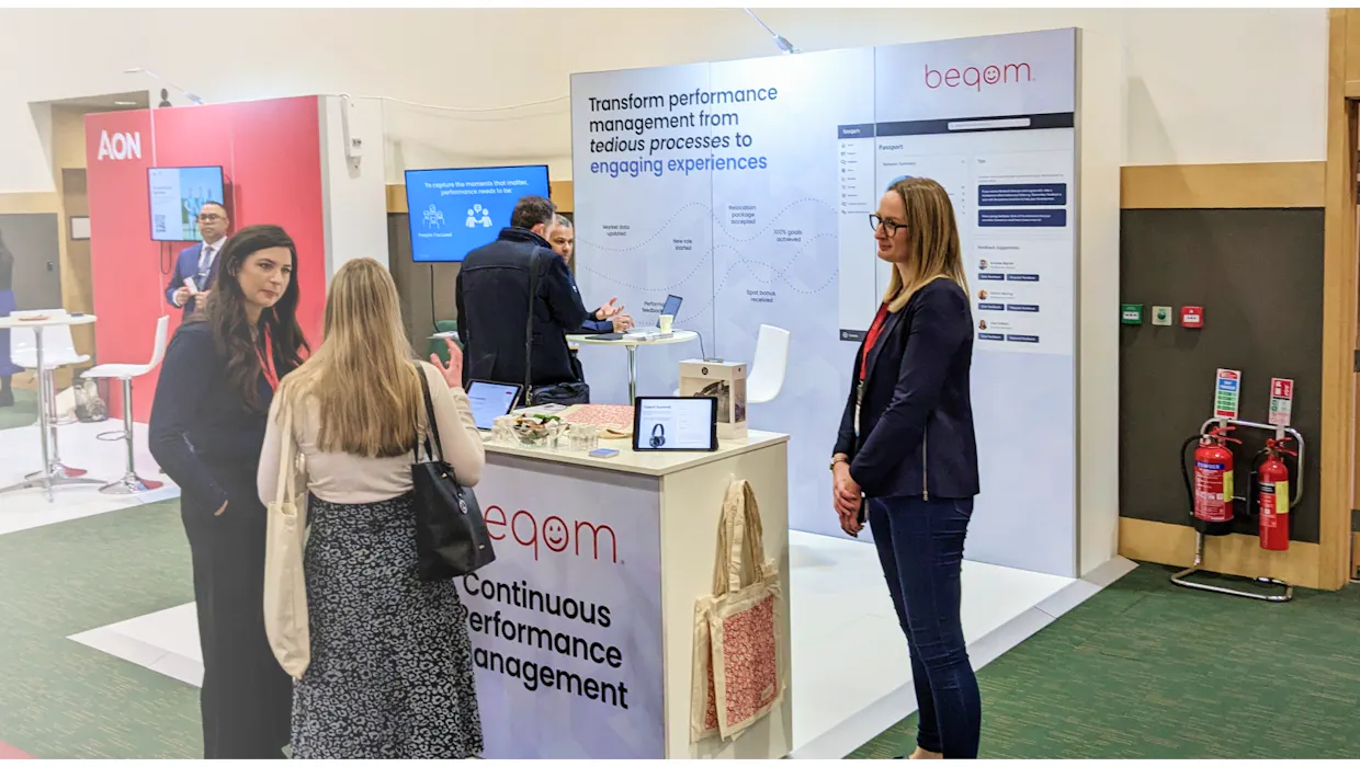 People talking at an event in front of beqom's booth