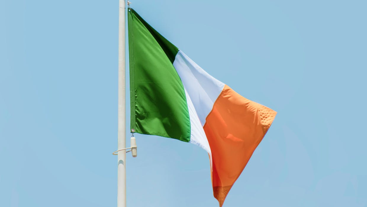 A photo of the Irish flag with a blue sky in the background.
