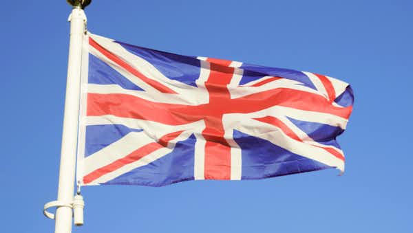 Union Jack flag, with red, white, and blue intersecting crosses, flying from a white pole against a clear blue sky.
