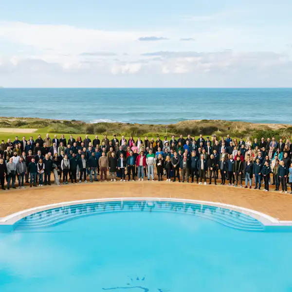 Eine große Gruppe von Menschen in Anzügen posiert an einem Pool vor dem Meer.