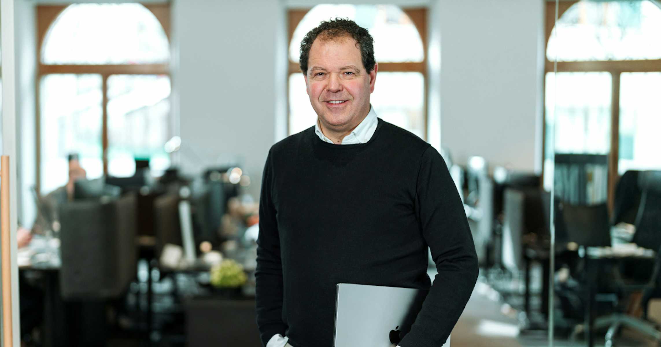 man in office setting with laptop under his arm