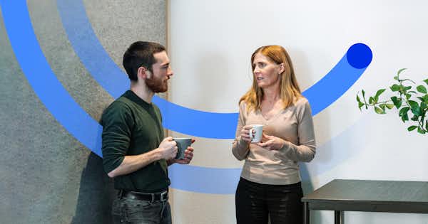 A man and a woman in an office setting having a conversation holding coffee cups.