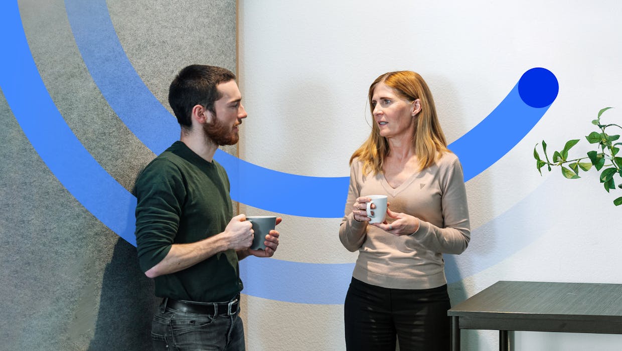 A man and a woman in an office setting having a conversation holding coffee cups.