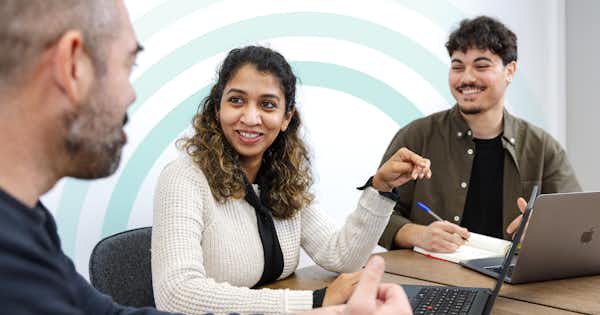Three people in a conference room talking.