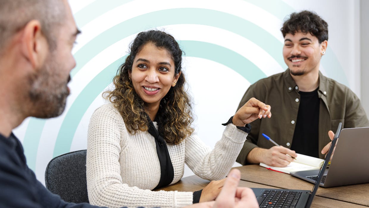Three people in a conference room talking.