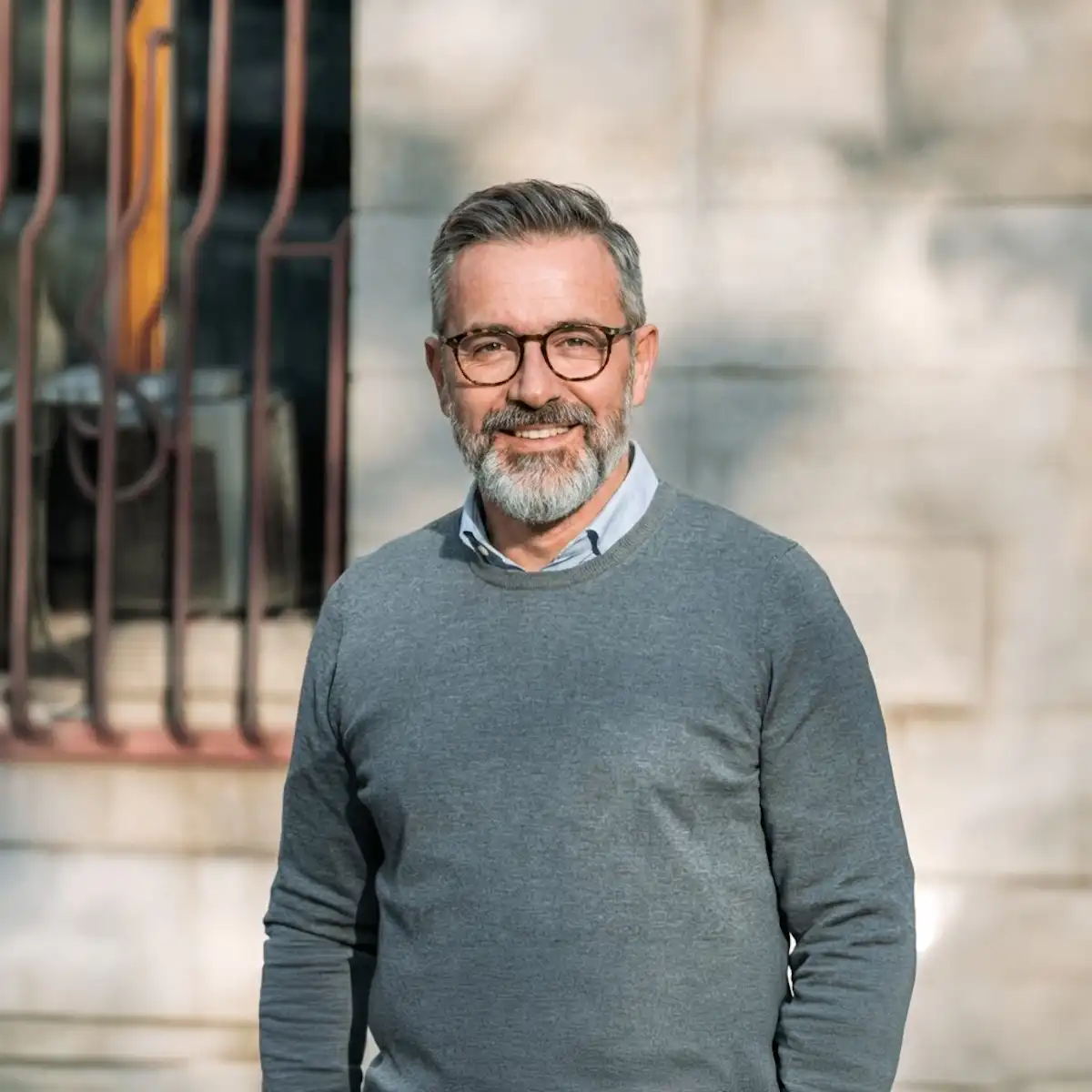 A photo of a man wearing a gray sweater looking into the camera.