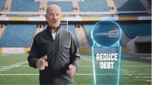 Bill Cowher on a football field next to a display that reads Reduce Debt