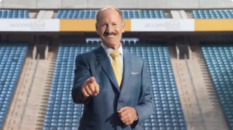 Bill Cowher in a suit and tie pointing at the camera in an empty stadium