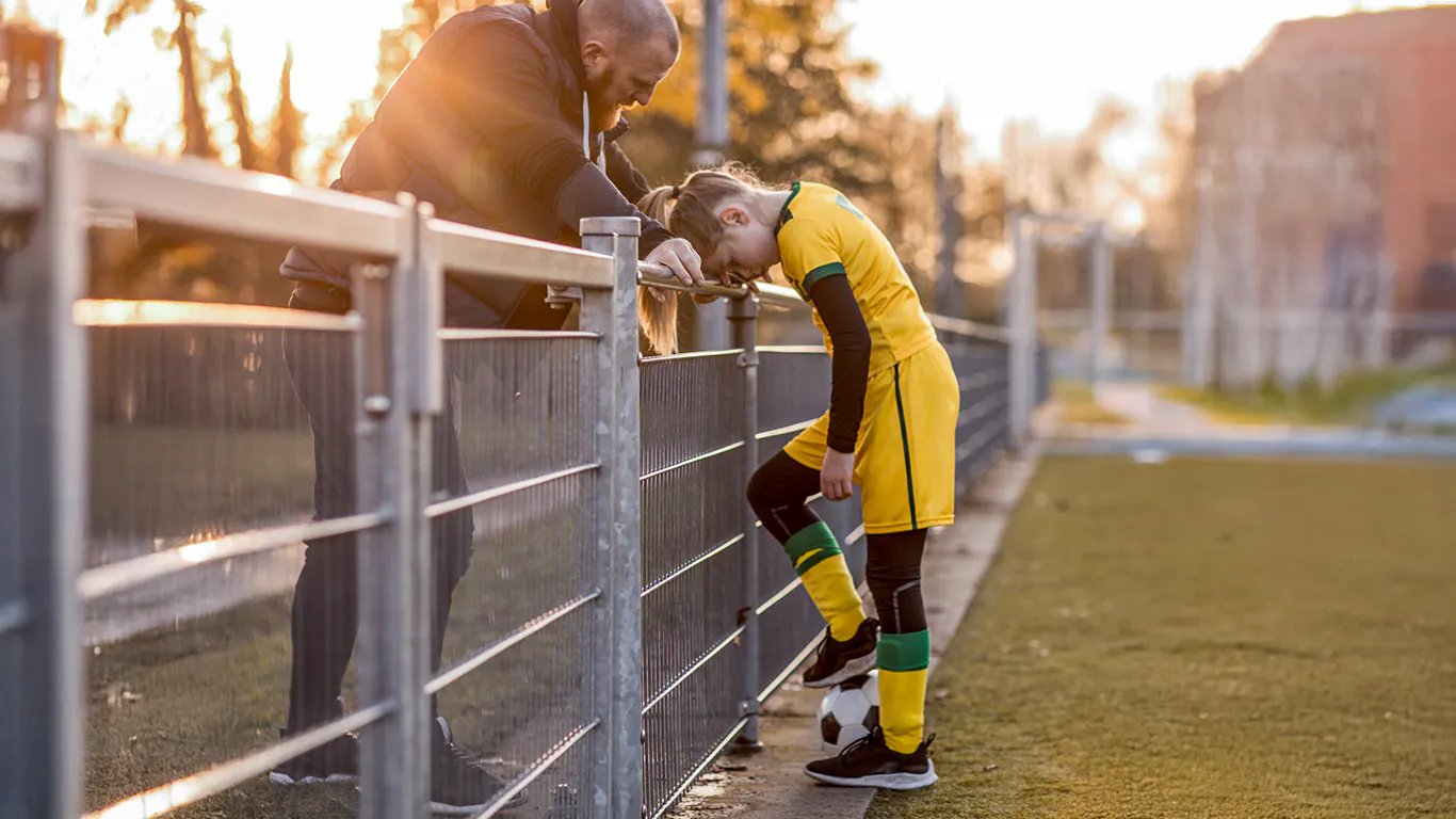 A father talking to his upset daughter on a soccer field