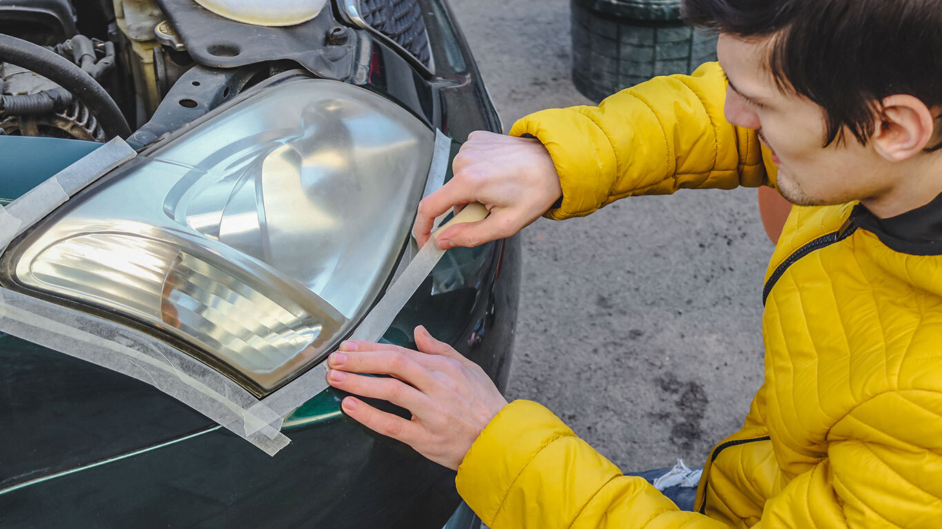 A young man taping up a damaged car headlight rather than paying for a repair