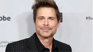 Rob Lowe in a dark pinstriped blazer, smiling slightly, at an event