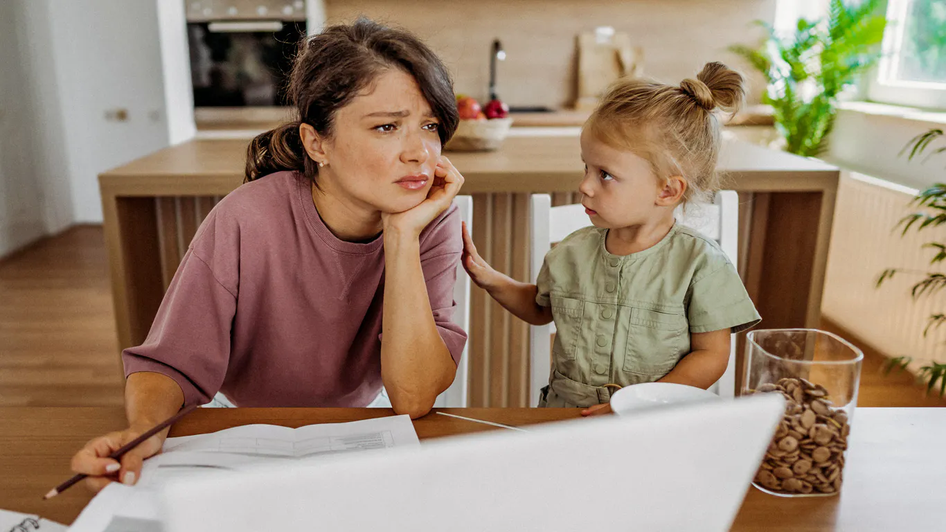 A parent looking stressed while reviewing bills at the kitchen table