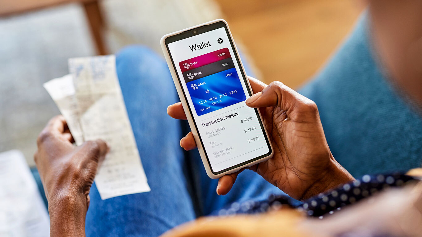 A person holding paper receipts while checking card balances and recent transactions on their phone