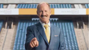 Bill Cowher in a suit and tie pointing at the camera in an empty stadium