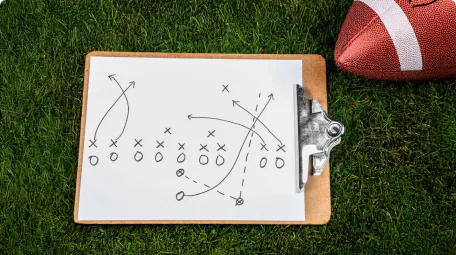 Clipboard with a football play diagram on the grass next to a football