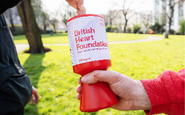 A person putting money into a British Heart Foundation collection tin