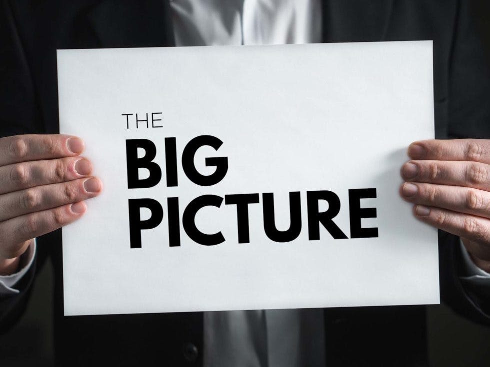 A man holding up a sign that says "the big picture"
