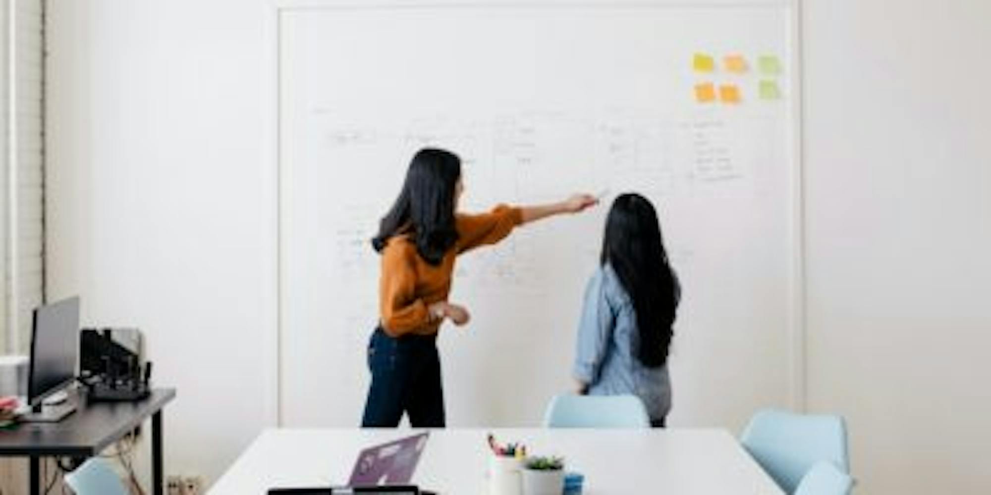 Women in a conference room discussing something on a board