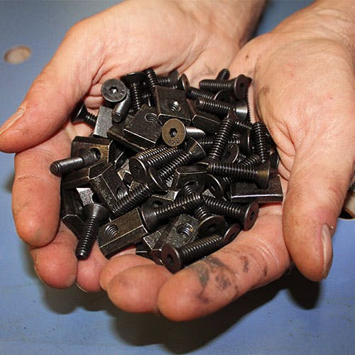 A pair of hands full of assorted and dirty bolts