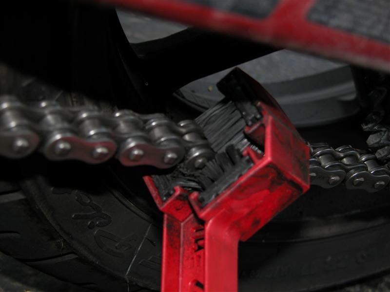 A red chain brush cleaning a motorcycle chain