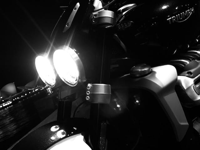 Black and white photo of headlights on Triumph Rocket 3R lit up with the Opera House behind it
