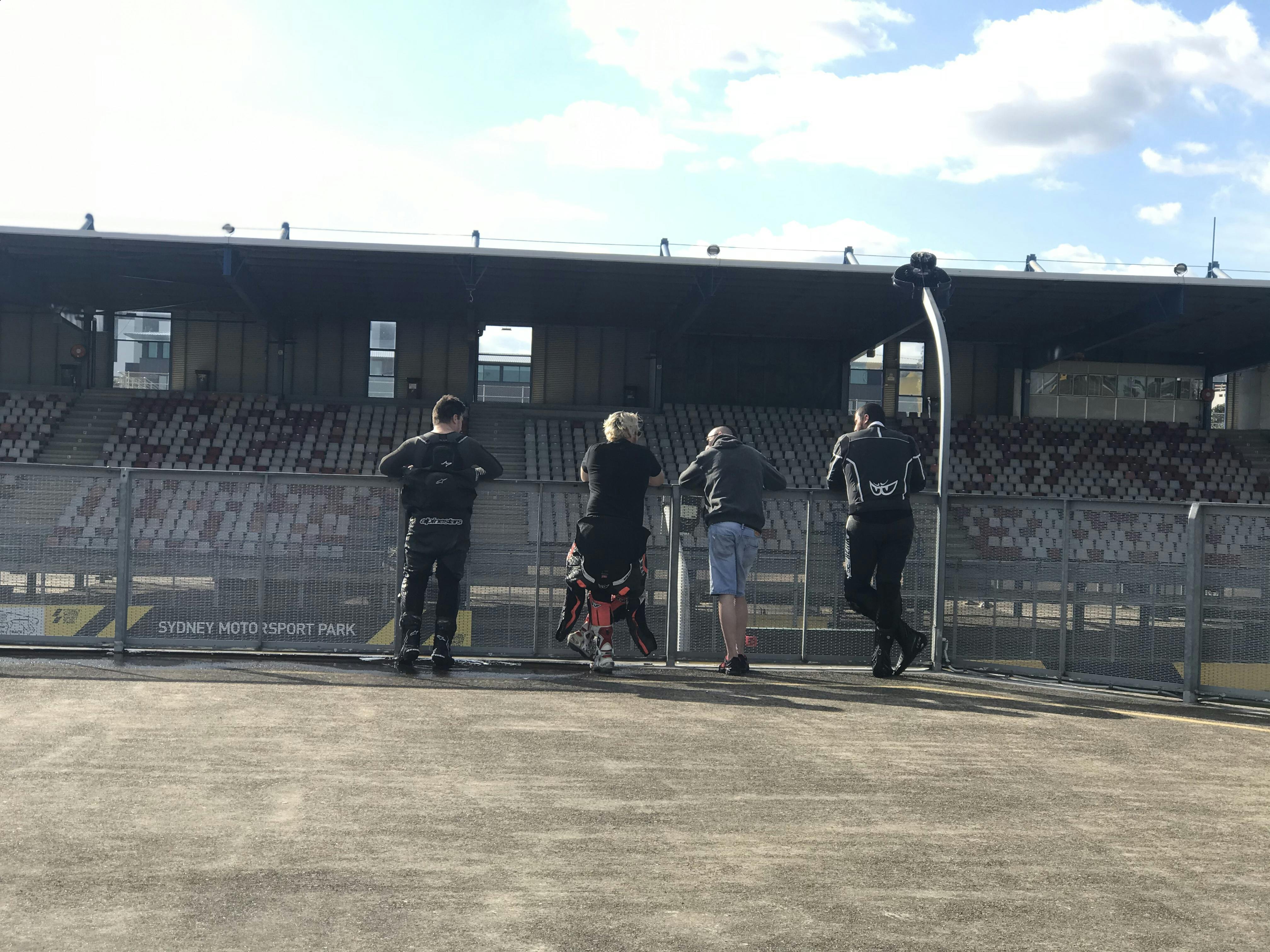 4 guys watching motorcycles on a track