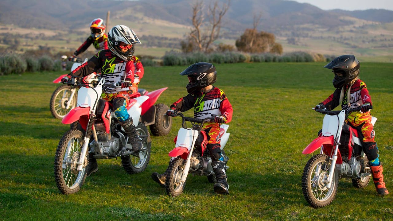 2 kids and 2 adults in motocross gear on red Honda dirt bikes