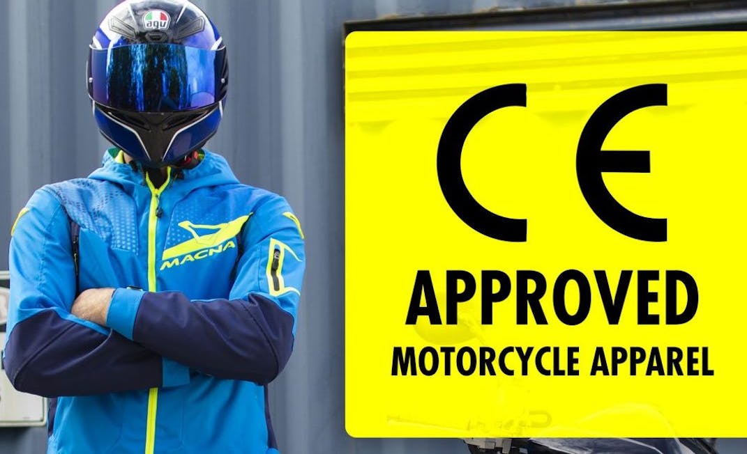 A guy in a AGV helmet and a blue Macna jacket next to a CE approved sign