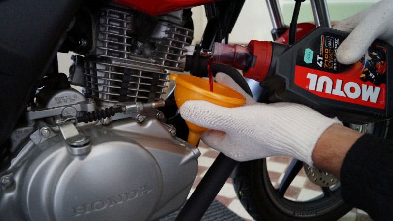 Gloved hands pouring oil into a motorcycle using a orange funnel