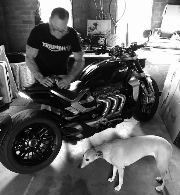 Man in a garage with a dog and a triumph Rocket 3 R motorcycle