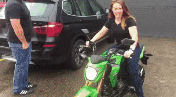Woman riding a Kawasaki Z125 motorcycle around a car park