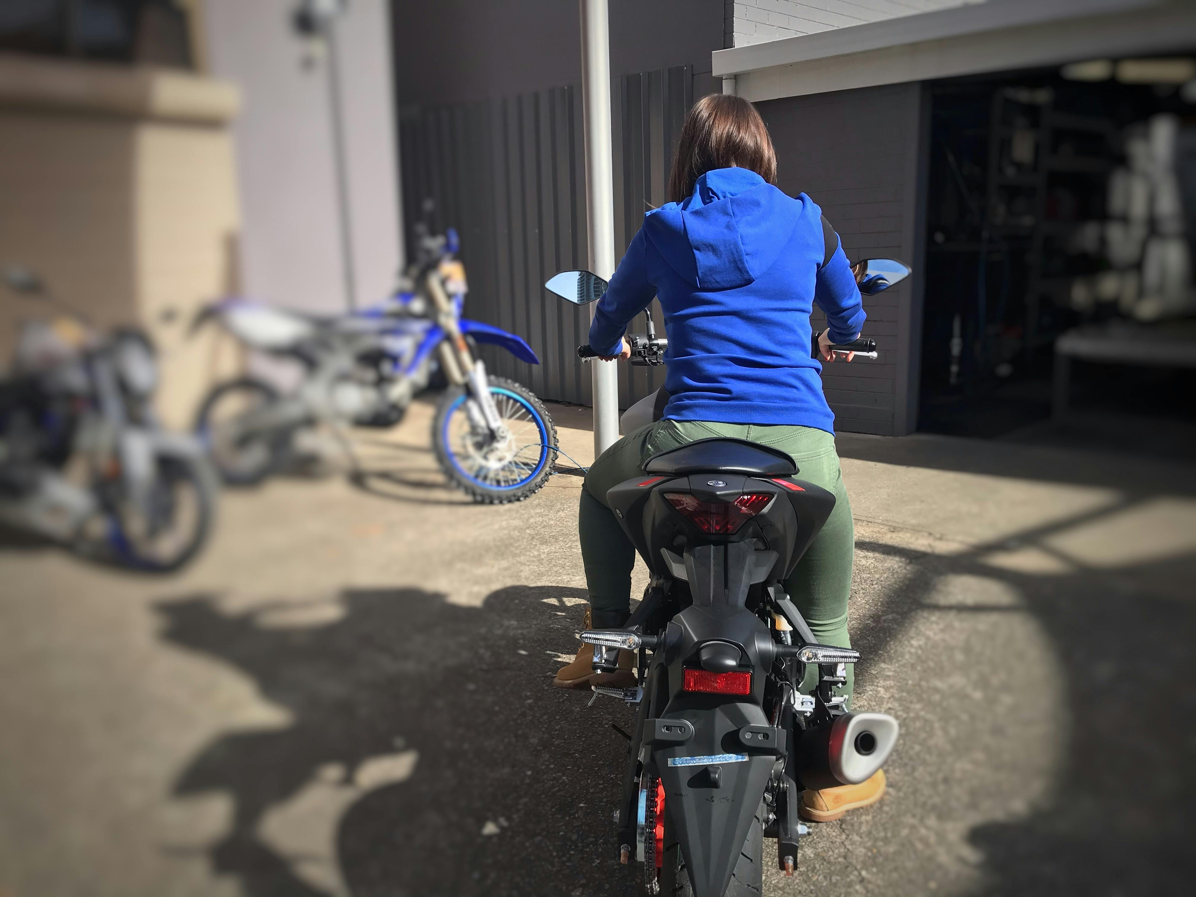 Woman in green pants sitting on a Yamaha MT03 in a car park