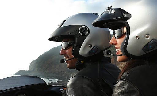 The Cardo Intercom System on a male rider with a dark silver open face helmet, and a female passenger with a light silver open face helmet