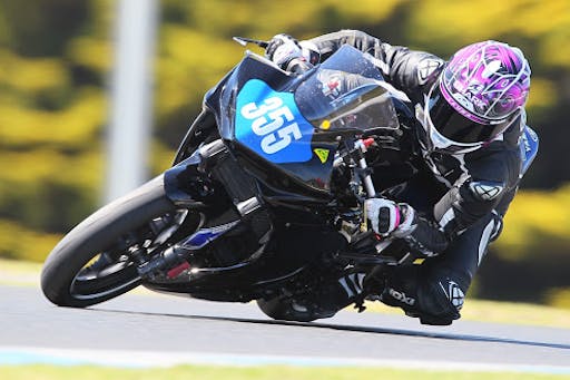 Woman on black motorcycle with pink helmet racing