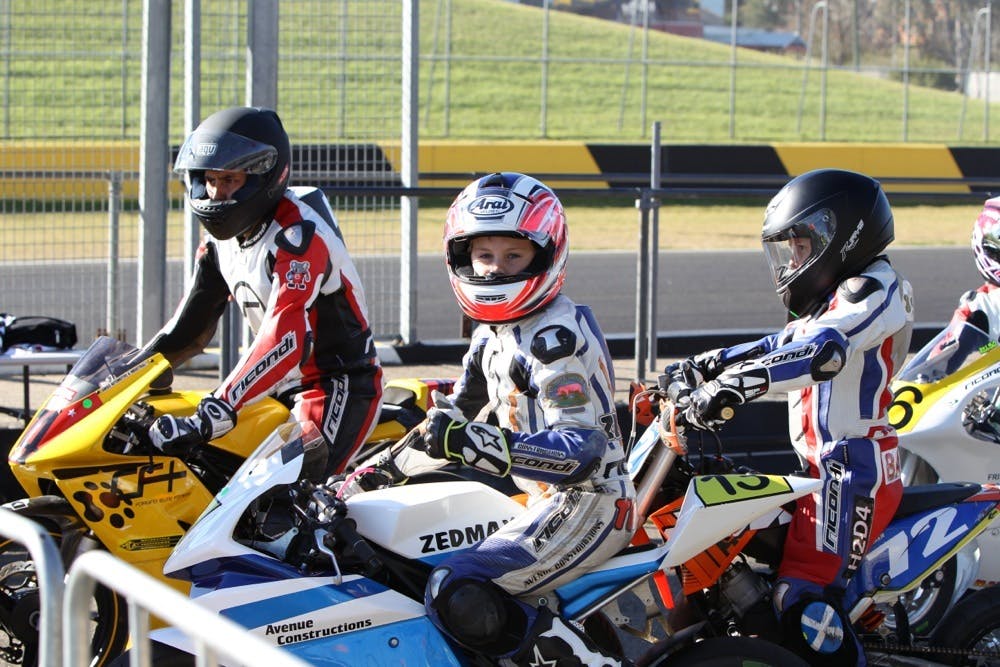 3 young boys on motorcycles in full protective gear at a racetrack