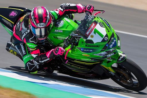 woman in pink and black leather racing a green motorcycle