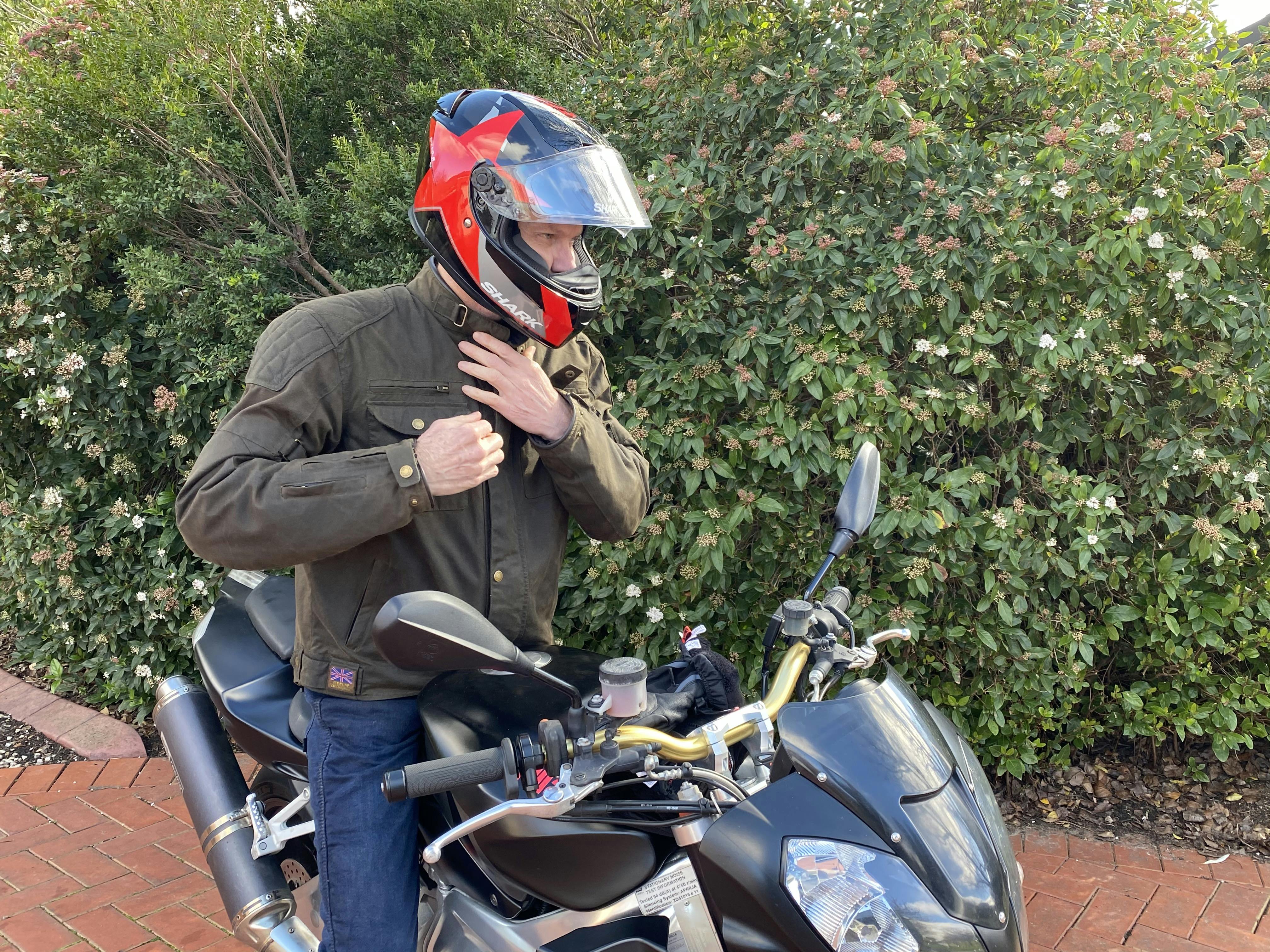 Man wearing the wax cotton Barton jacket by Merlin on a motorcycle with a red helmet