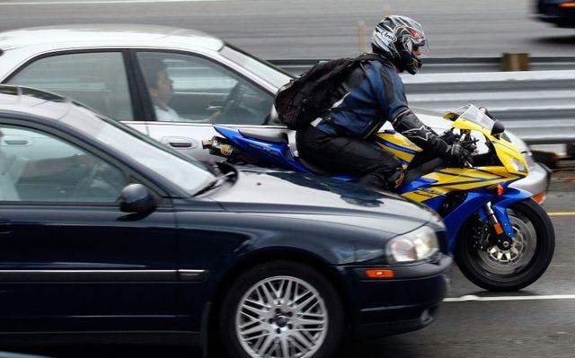 A motorcycle lane filtering in front of 2 cars