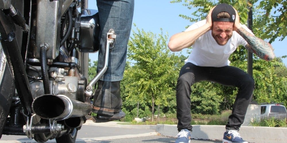 Guy covering his ears next to a motorcycle 