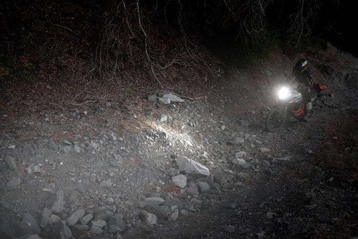 An adventure motorcycle on a dirt road with a bright headlight
