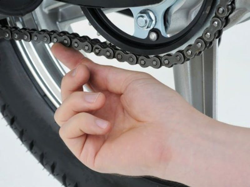 a hand checking the slack in a motorcycle chain