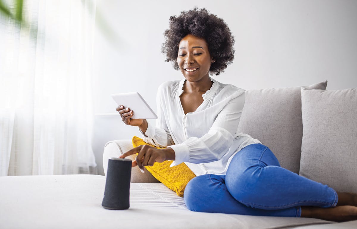 Vaut-il la peine d'intégrer une technologie intelligente lors de la rénovation Femme assise sur un canapé jouant de la musique sur un haut-parleur intelligent