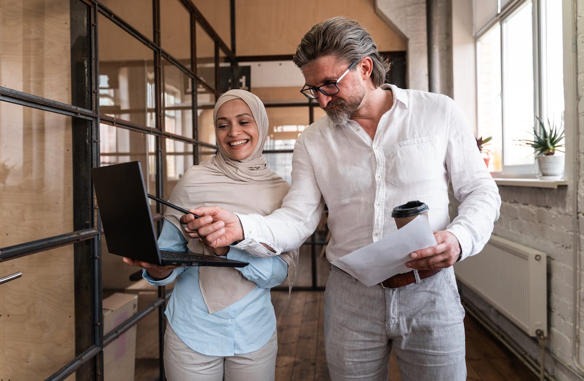 Femme portant un hijab aidant un homme sur son laptop à faire de la recherche