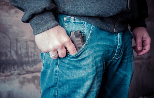 Man holding a gun in his jean pocket - Photo by Bermix Studio on Unsplash