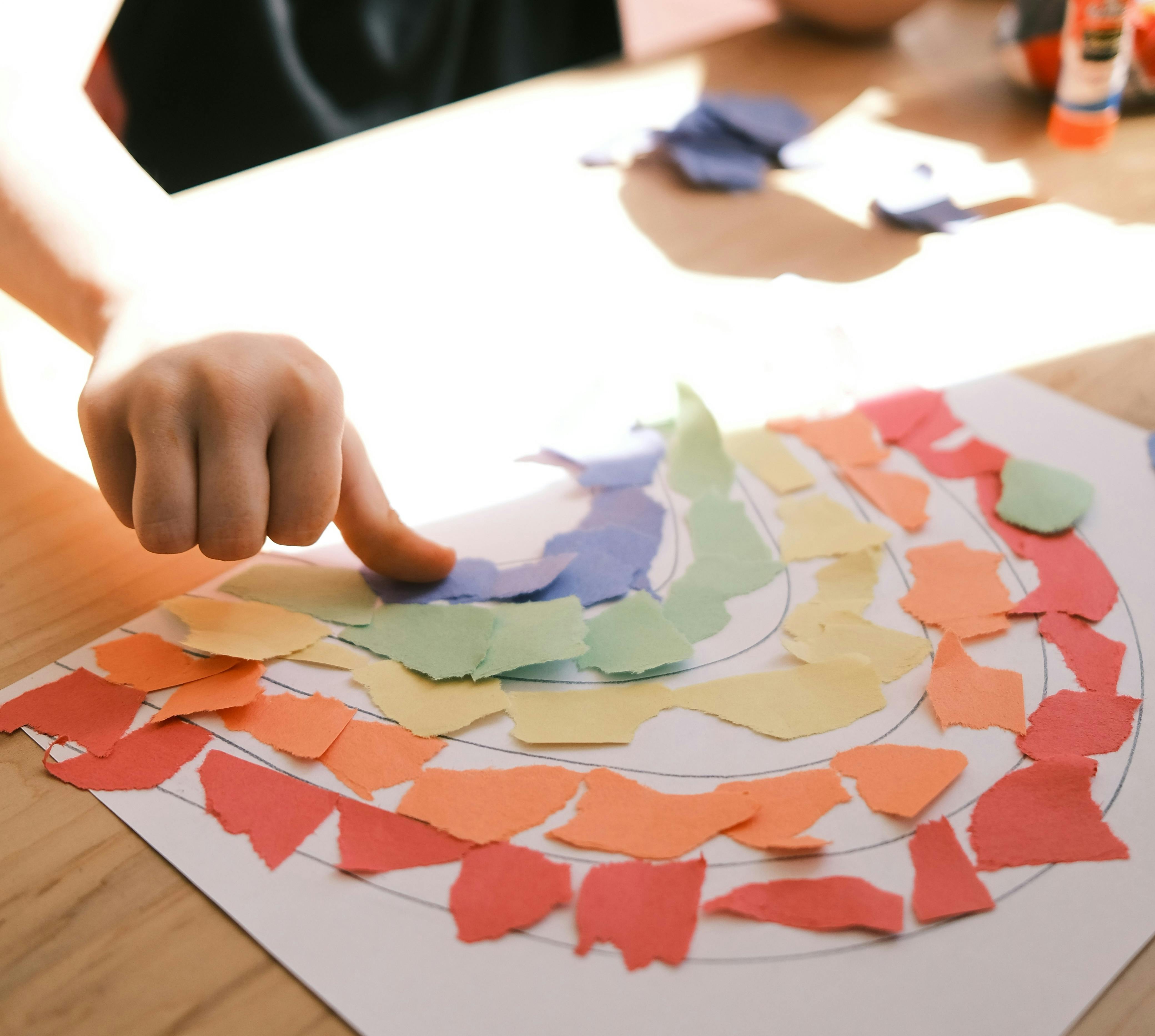 child making rainbow out of torn construction paper pieces 