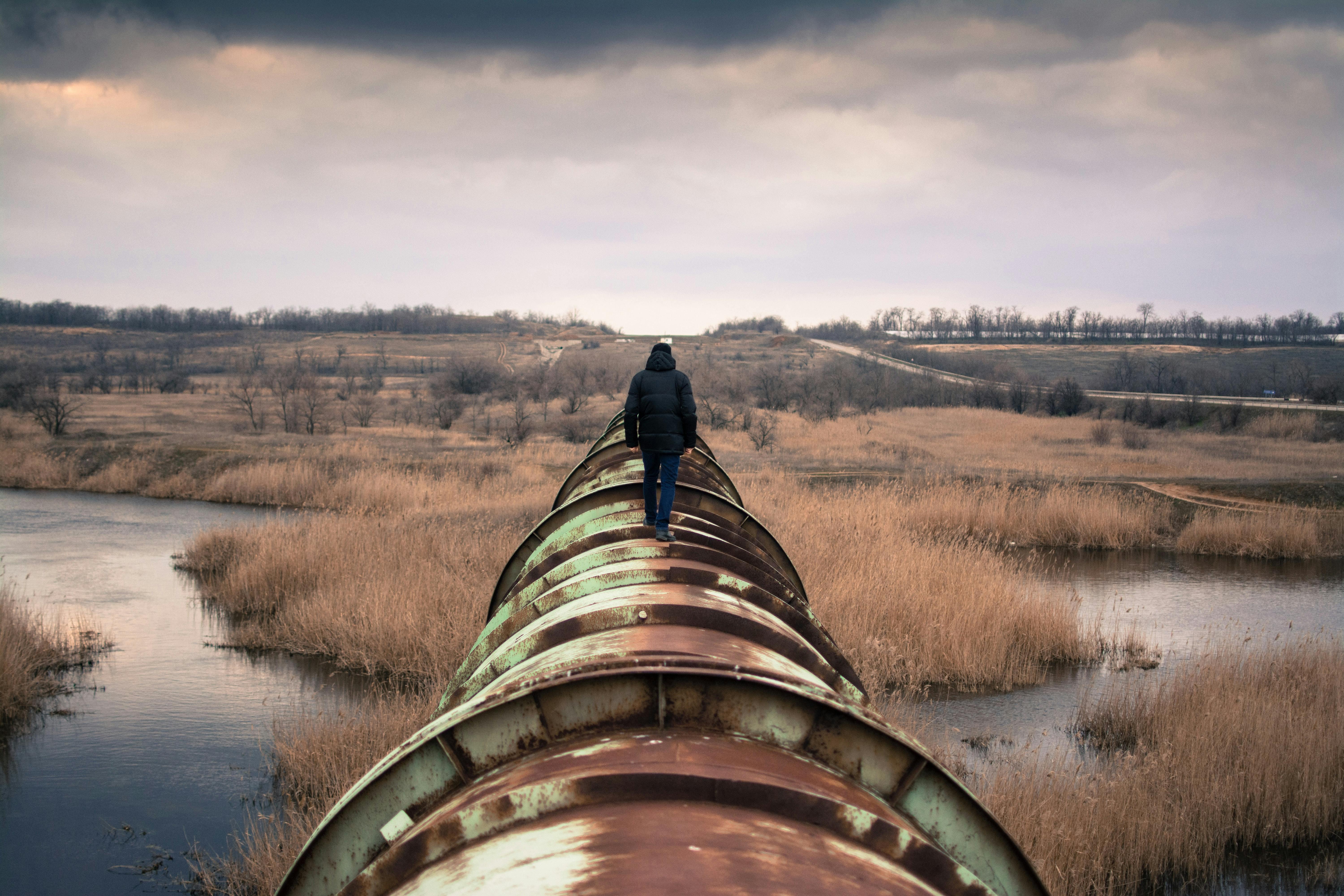 person walking on an oil pipeline in the flatlands - Photo by Rodion Kutsaiev on Unsplash